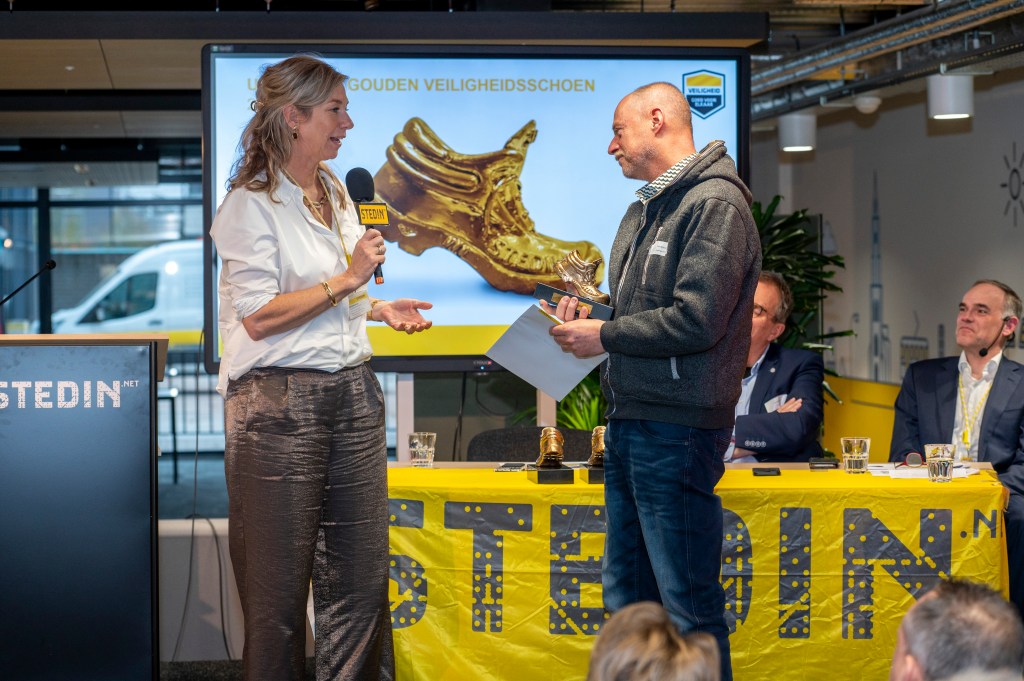 Dick ontvangt de gouden veiligheidsschoen en juryrapport uit handen van Trudy Onland